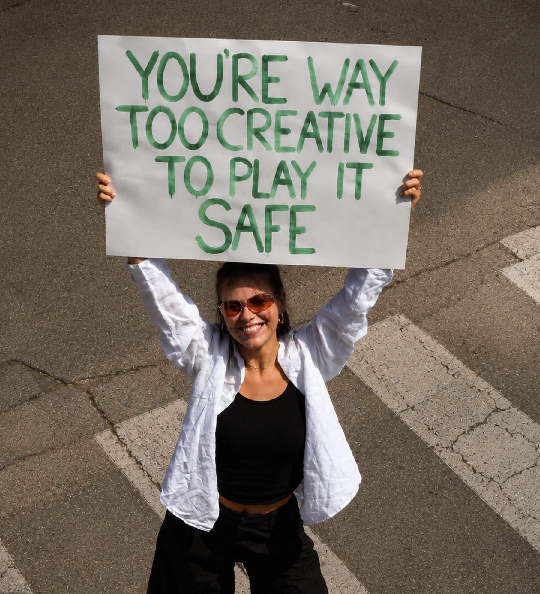 Charisia houdt midden op een zebrapad een bord omhoog: you're way too creative to play it safe